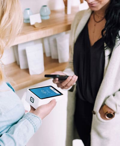 A woman holding a white payment box while another woman holds her phone up to it