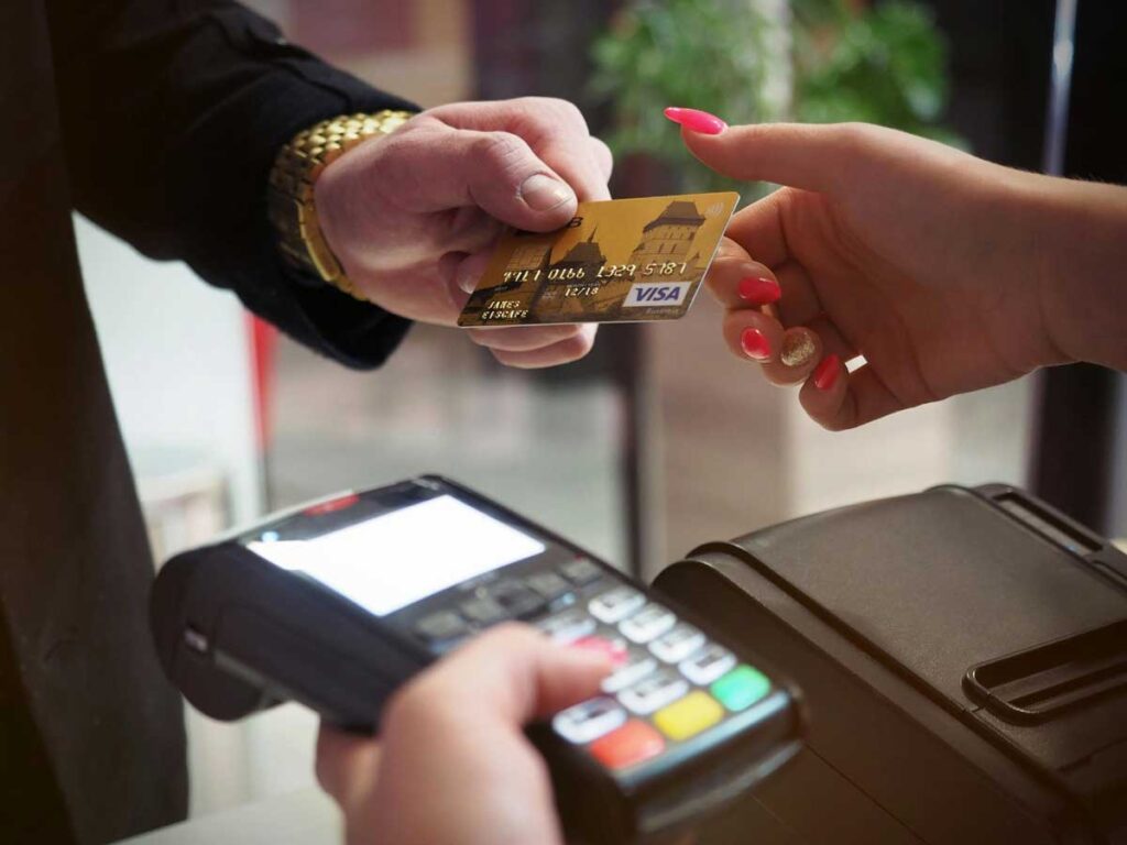 Customer with gold watch handing his Visa payment card to a vendor holding a card reader.