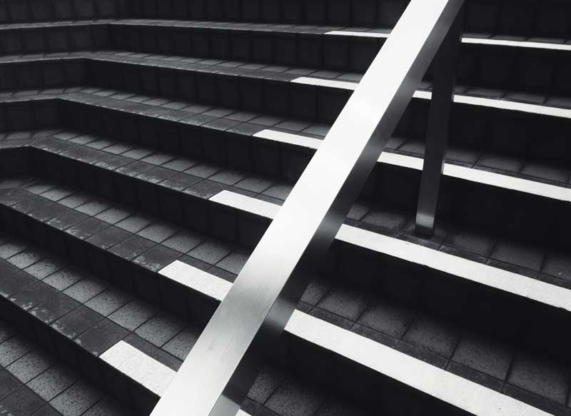 Modern-style image of a silver and black ascending staircase with a bright metallic handrail in the center.