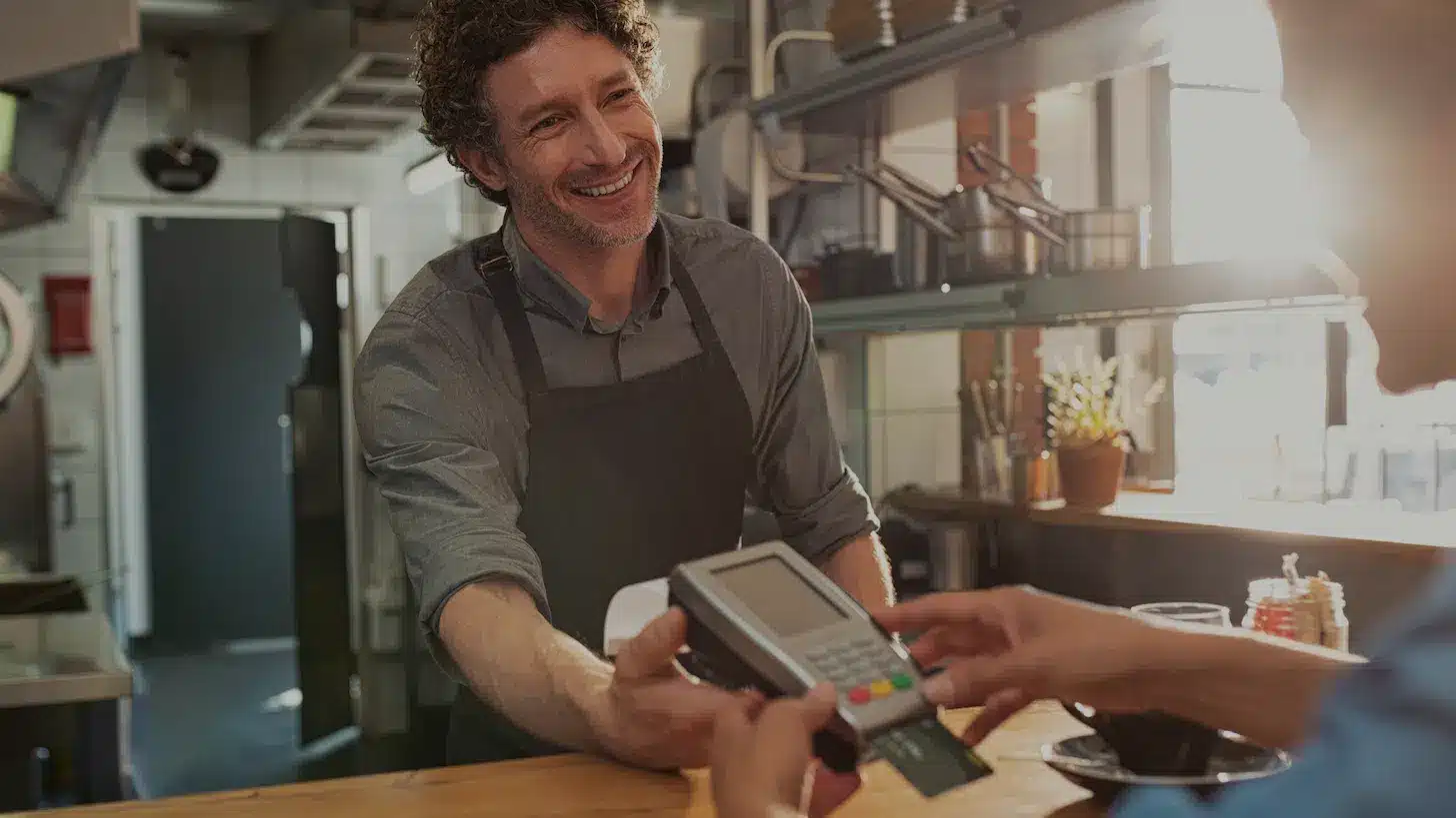 a smiling merchant accepting credit card payment from a customer