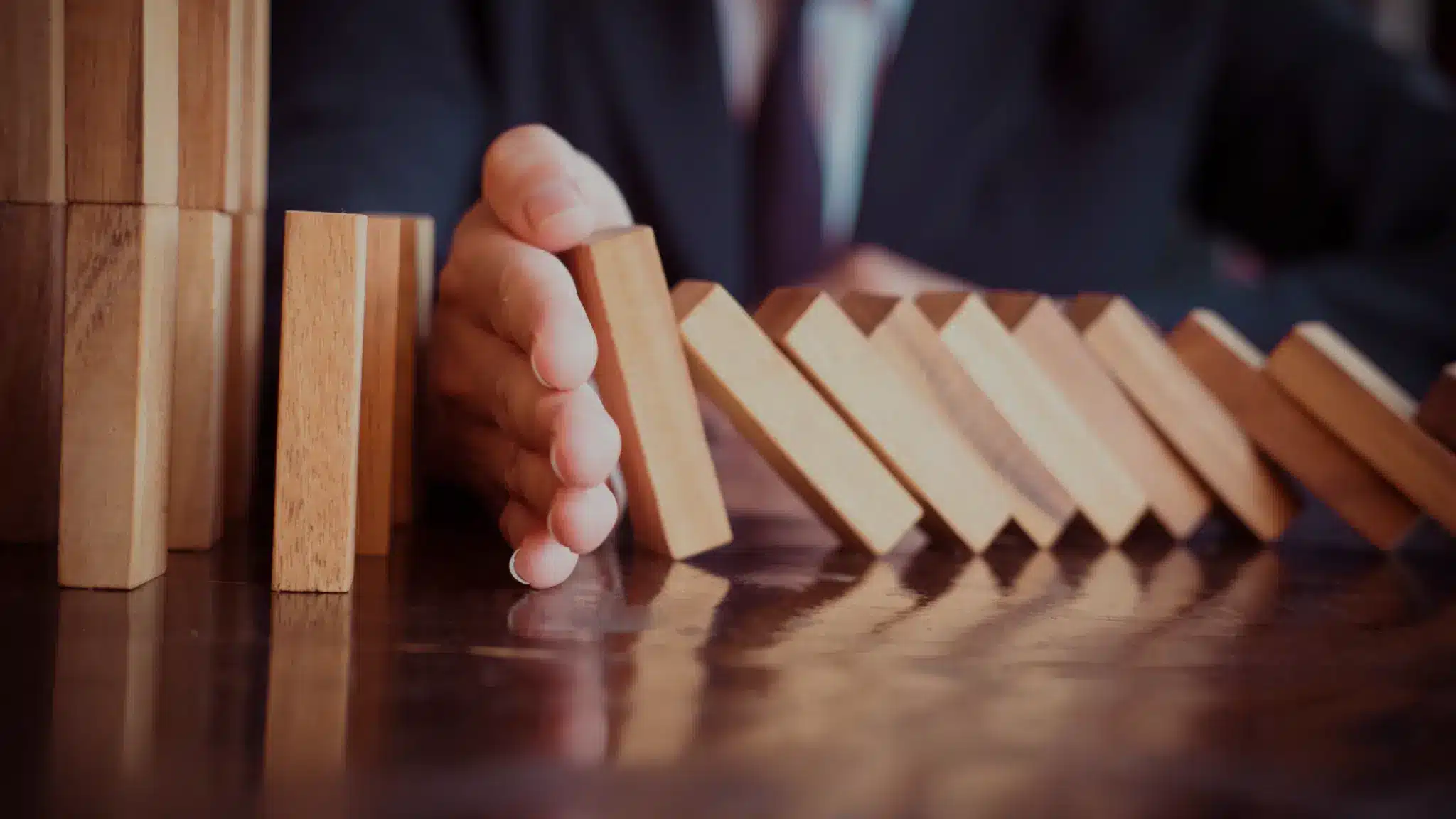 a hand stopping domino bricks from tipping over