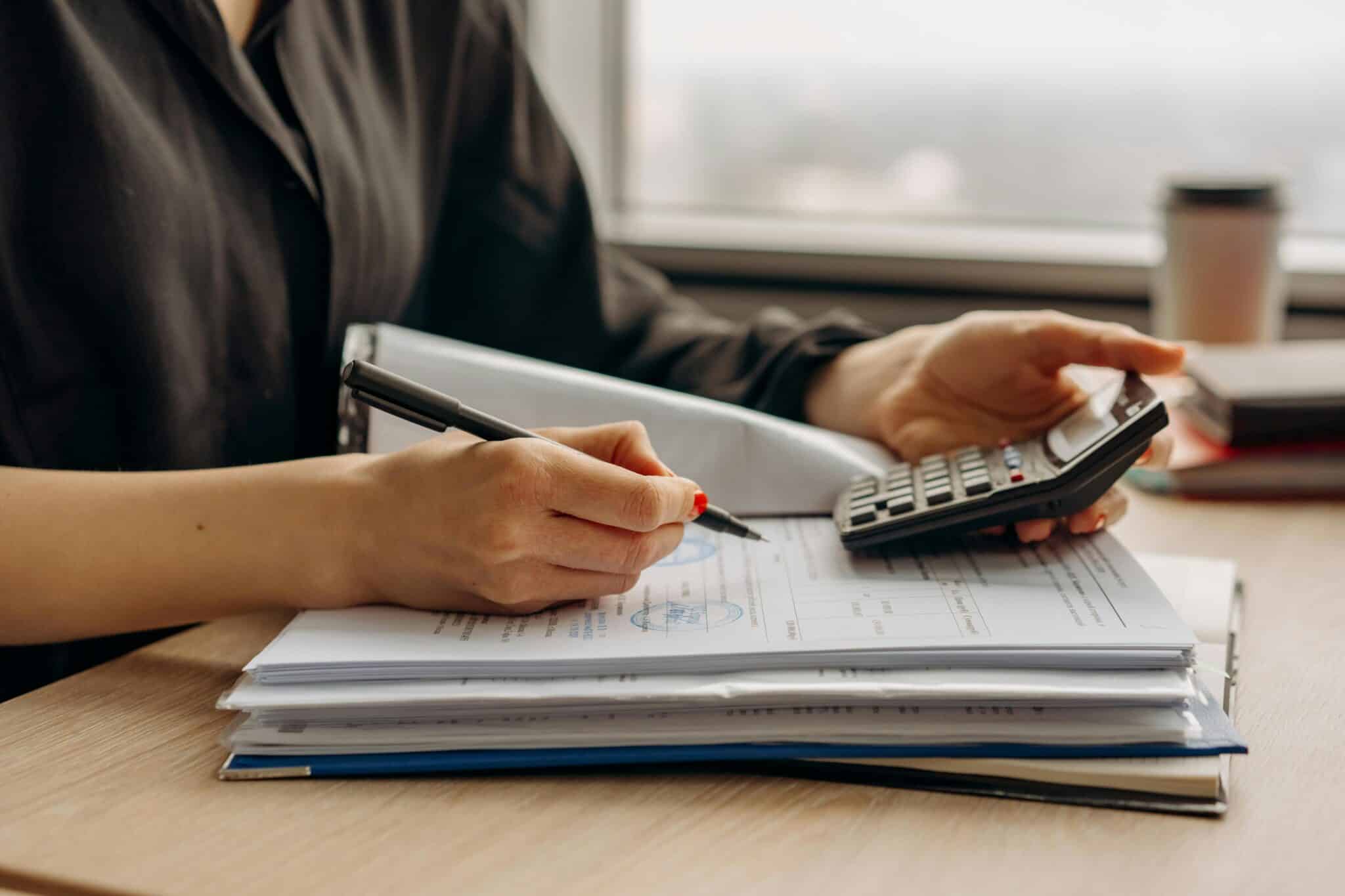 An accountant using a calculator to complete a transaction and holding a pen to note the result.