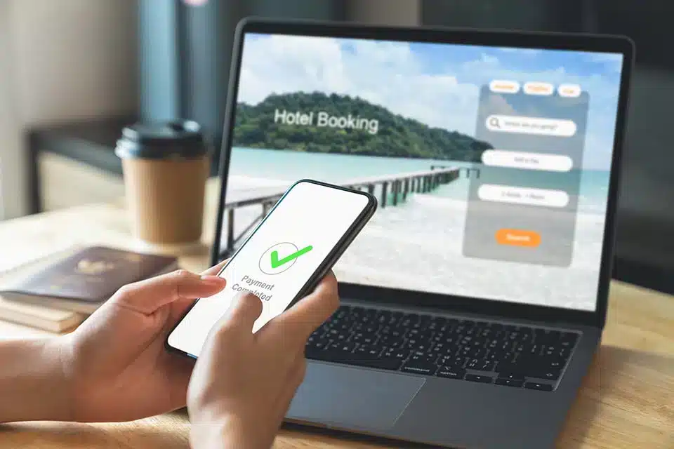 a phone showing "payment confirmed", a laptop in the background on a hotel booking website