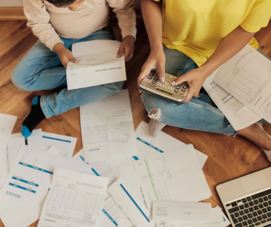 two people looking at paperwork on the floor while holding a calculator