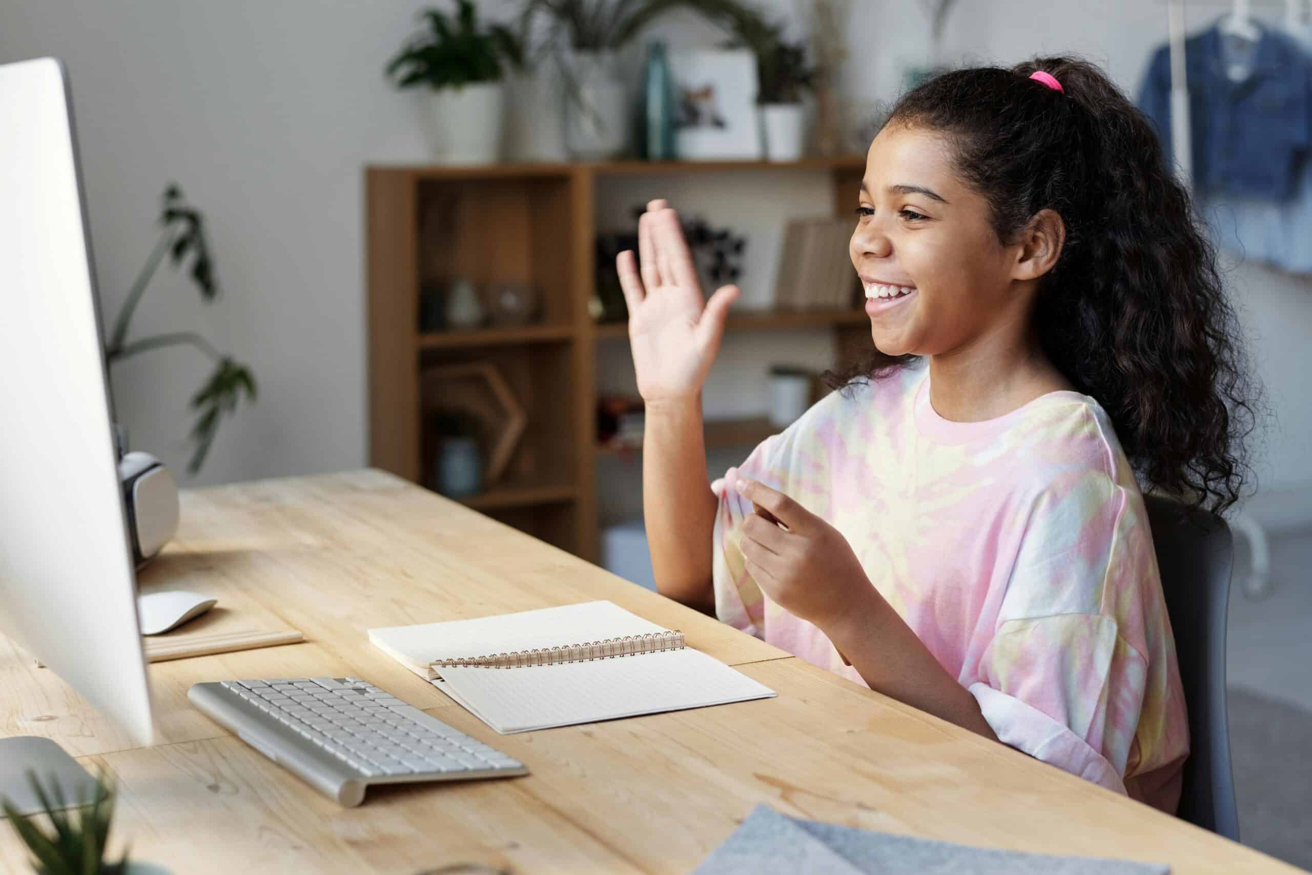 Student using e-learning platform and raising hand in front of computer
