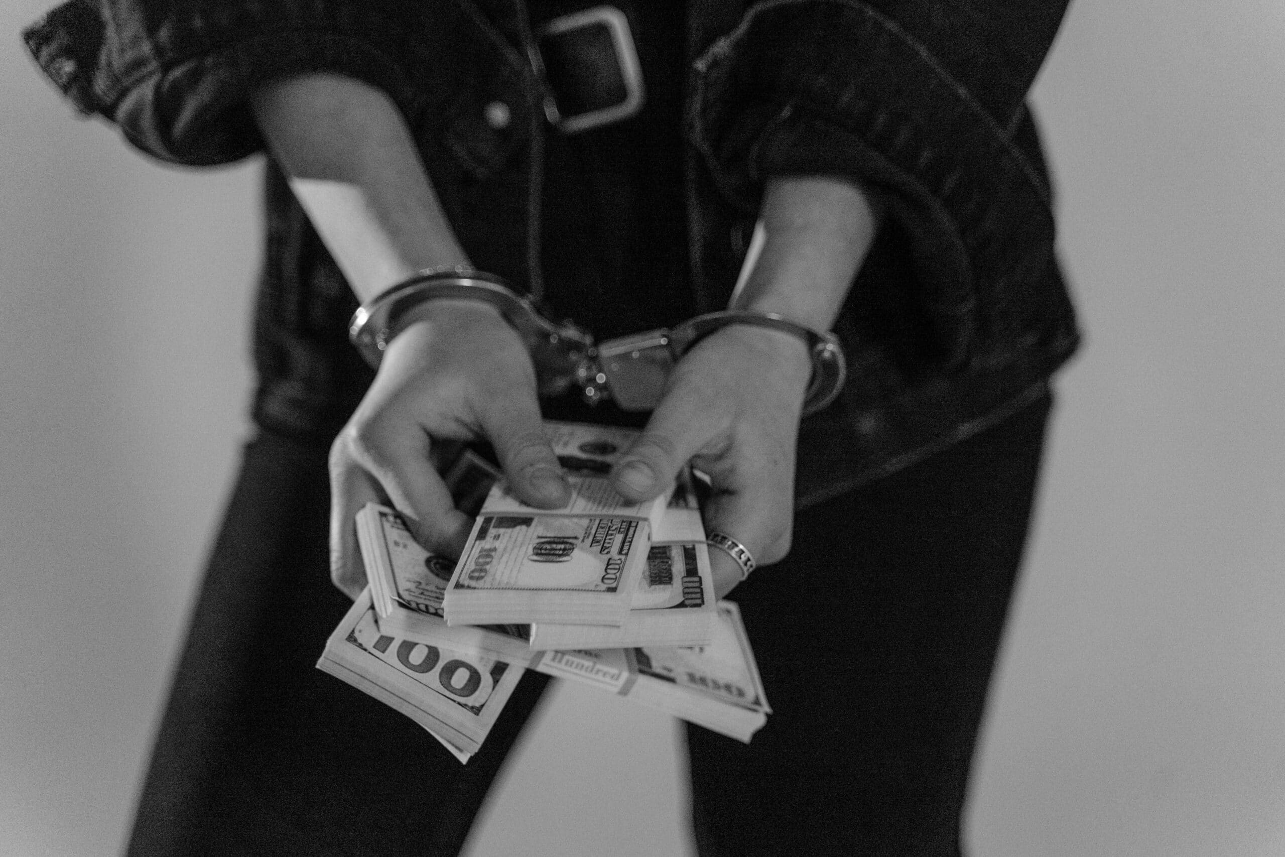 Person with handcuffs holding stacks of dollar bills