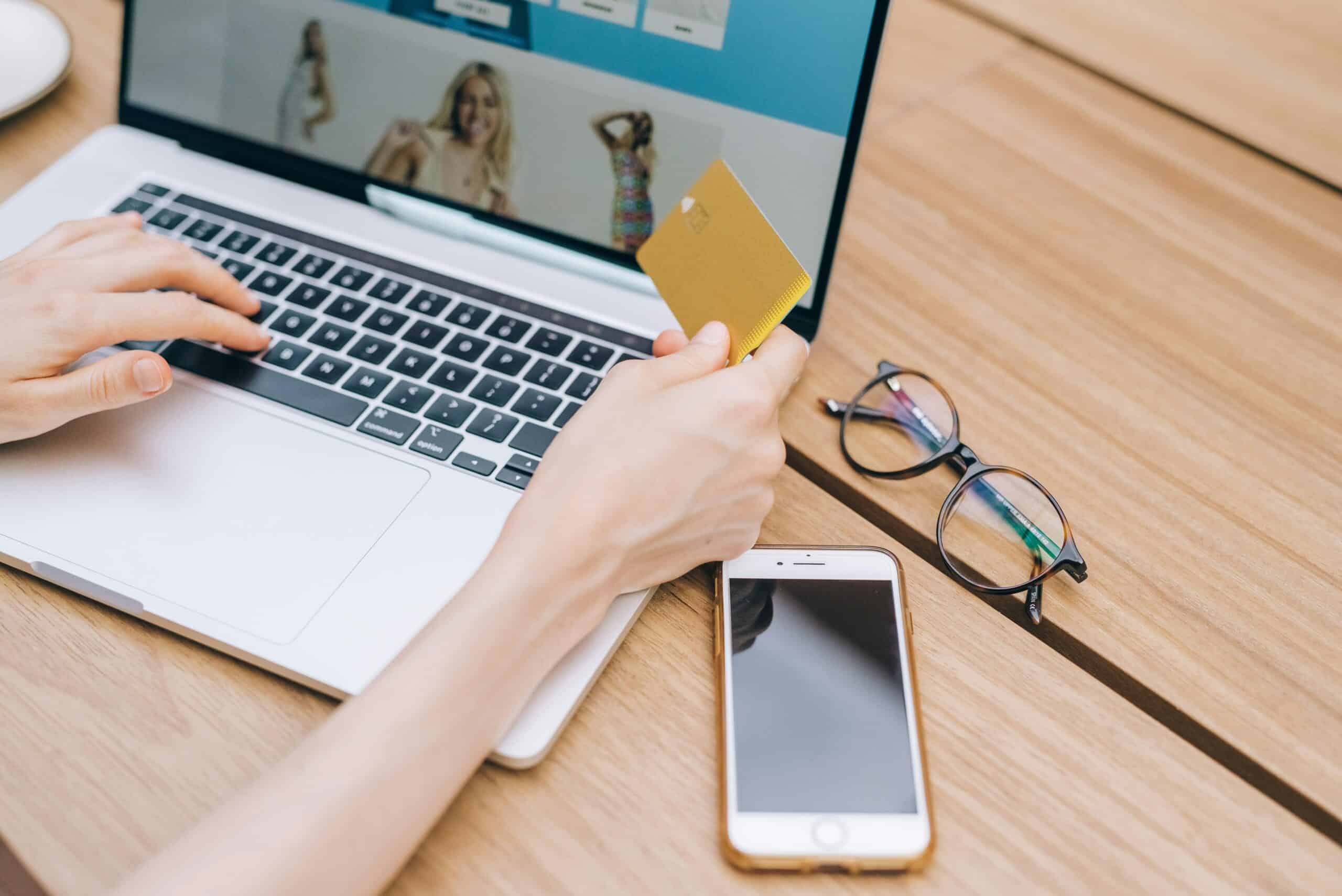 A person holding a credit card up to their laptop computer screen to complete a purchase on an online POS screen