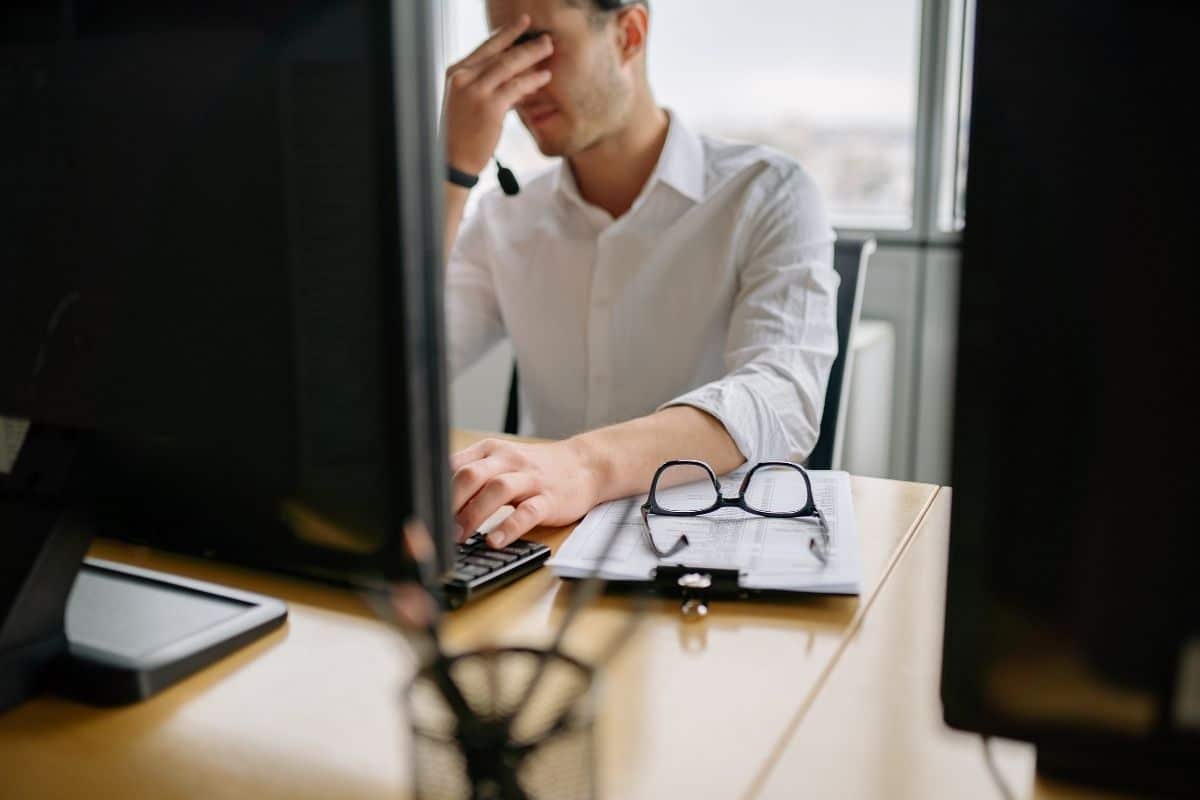 a man pressing against the bridge of his nose in frustration in front of a computer