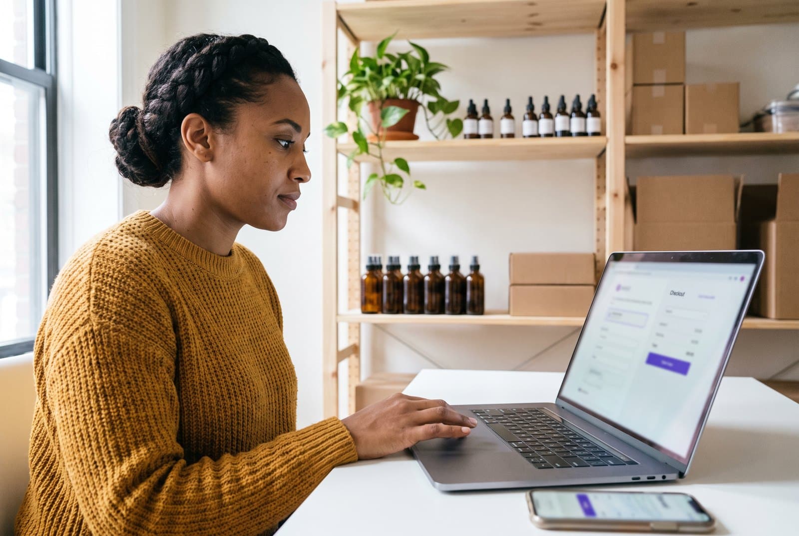 CBD store owner testing her WooCommerce checkout on a laptop with tincture bottles and product boxes on the shelves behind her